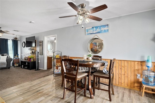 dining room with ceiling fan, light hardwood / wood-style flooring, and wooden walls