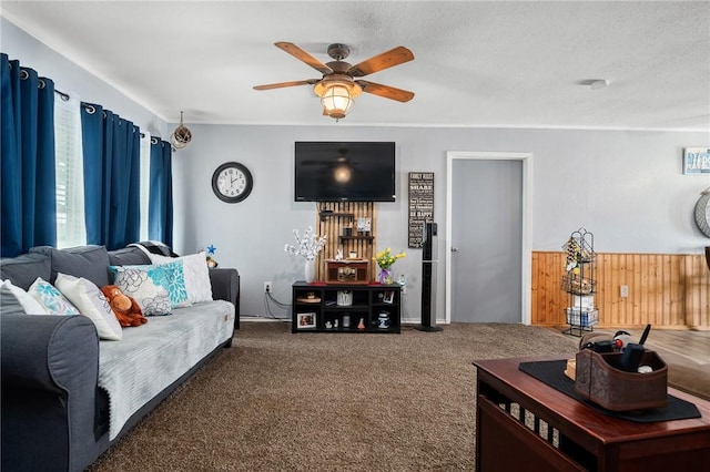 living room with wooden walls, ceiling fan, a textured ceiling, and dark colored carpet