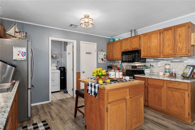 kitchen featuring appliances with stainless steel finishes, dark hardwood / wood-style floors, crown molding, and washer / dryer