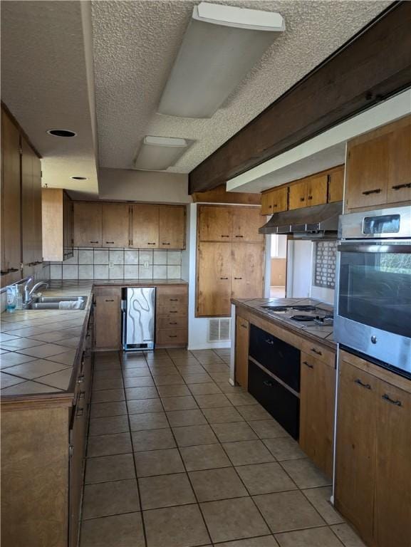 kitchen featuring light tile patterned floors, tile counters, oven, white gas stovetop, and sink