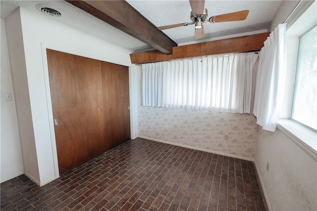 unfurnished room featuring a textured ceiling, ceiling fan, and beam ceiling