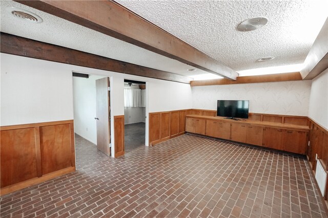 interior space with a textured ceiling, wood walls, and beamed ceiling