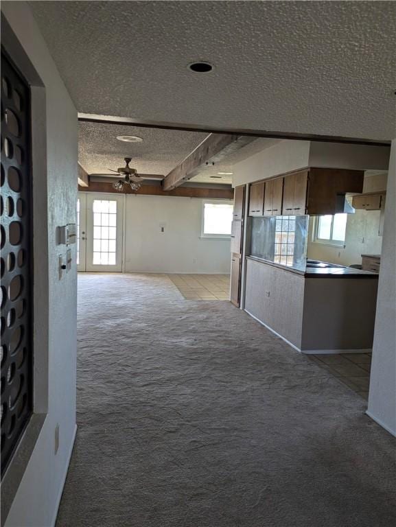 unfurnished living room with beam ceiling, light colored carpet, ceiling fan, and a textured ceiling