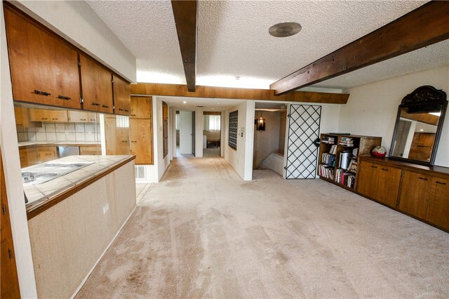 interior space with a textured ceiling, tile counters, beamed ceiling, tasteful backsplash, and light colored carpet