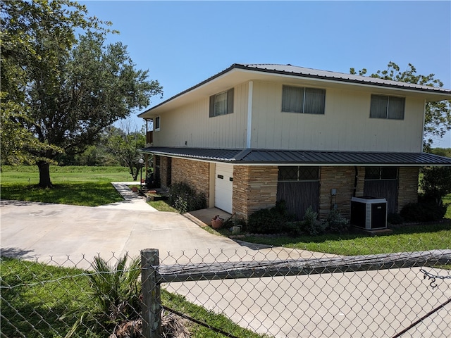 view of front of home with a garage, a front lawn, and central air condition unit