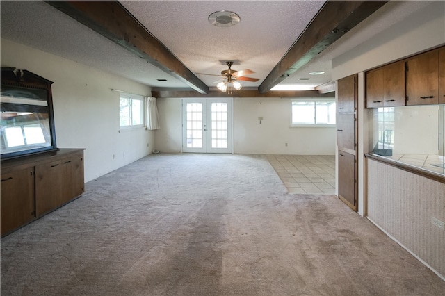 empty room with a textured ceiling, light carpet, beamed ceiling, french doors, and ceiling fan