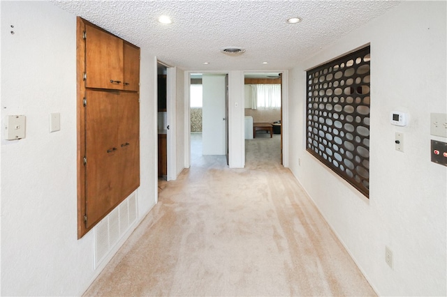 corridor featuring a textured ceiling and light carpet