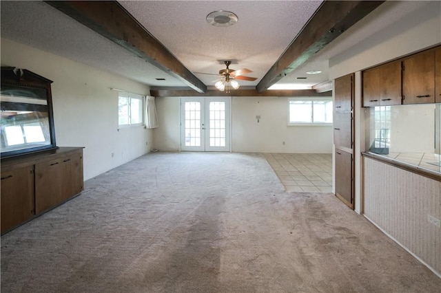 interior space with a textured ceiling, beamed ceiling, french doors, ceiling fan, and light colored carpet