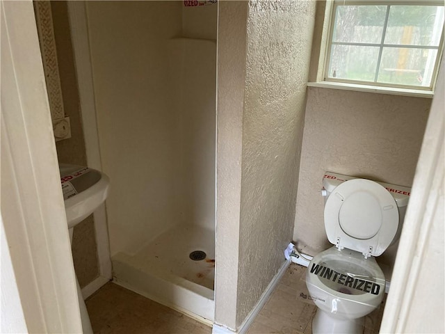 full bath with a textured wall, a stall shower, and toilet