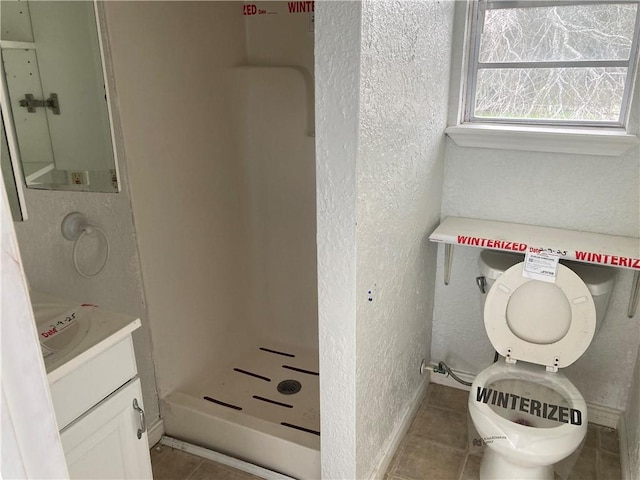 bathroom with a textured wall, vanity, baseboards, a shower stall, and tile patterned floors