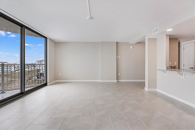 empty room with a wealth of natural light, a wall of windows, and light tile patterned floors