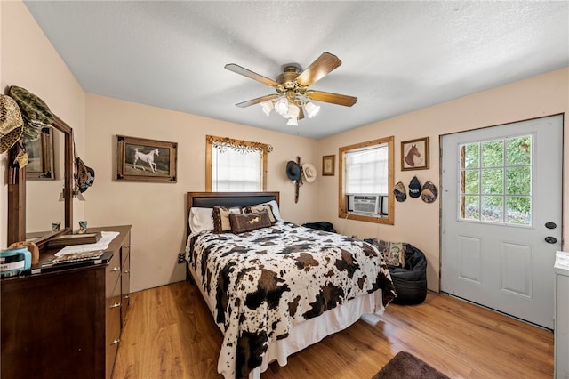 bedroom with light wood-type flooring, cooling unit, a textured ceiling, and ceiling fan