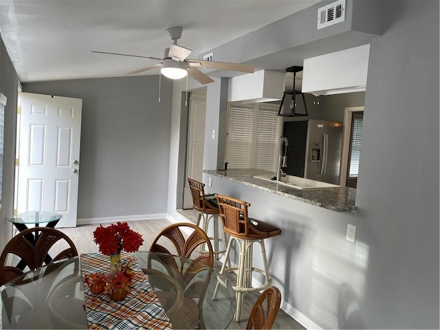 kitchen featuring stainless steel fridge, light hardwood / wood-style flooring, ceiling fan, light stone counters, and kitchen peninsula