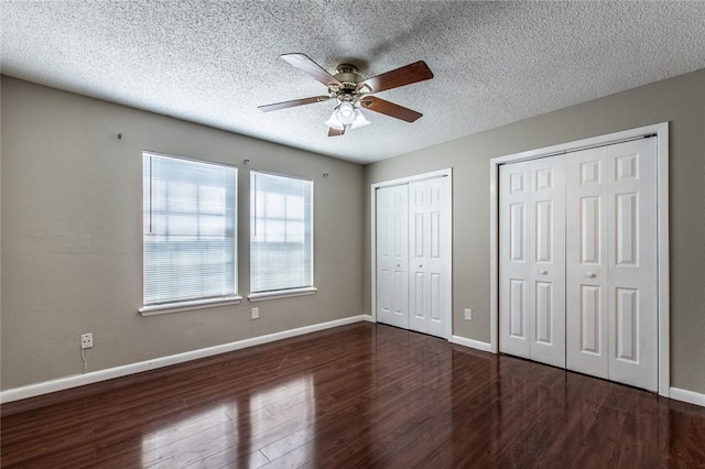 unfurnished bedroom with a textured ceiling, baseboards, multiple closets, and wood finished floors