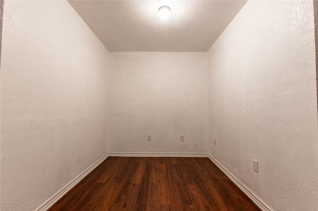 unfurnished room featuring baseboards, dark wood-type flooring, and a textured wall