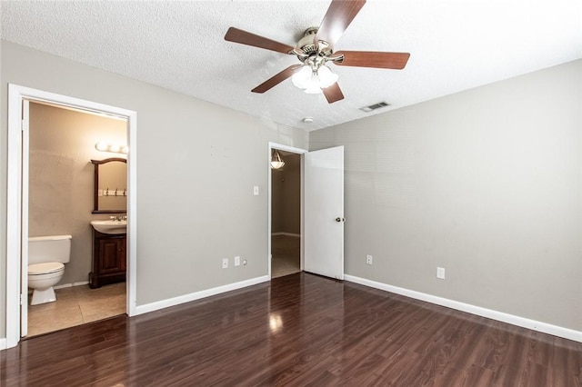 unfurnished bedroom with visible vents, ensuite bathroom, a textured ceiling, wood finished floors, and baseboards