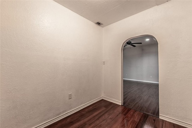 unfurnished room with dark wood-style floors, visible vents, baseboards, arched walkways, and ceiling fan