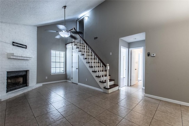 interior space with visible vents, a brick fireplace, ceiling fan, stairway, and tile patterned floors