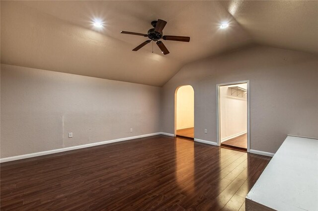 bonus room with baseboards, ceiling fan, vaulted ceiling, arched walkways, and dark wood-style floors