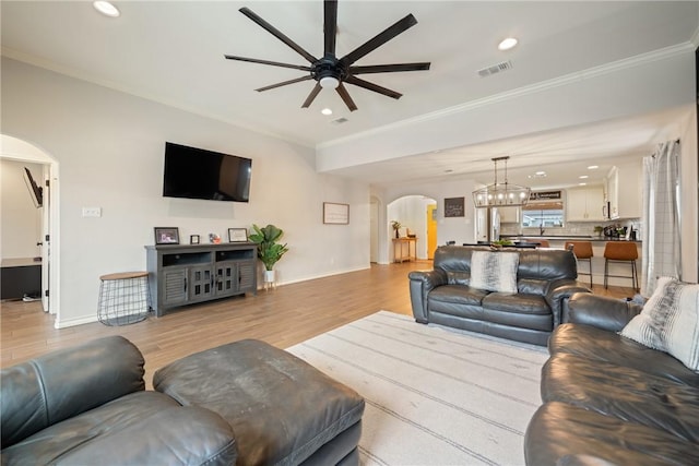 living room featuring ceiling fan with notable chandelier, crown molding, and light hardwood / wood-style flooring