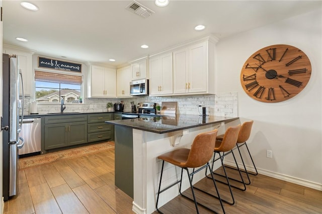 kitchen featuring sink, kitchen peninsula, appliances with stainless steel finishes, light hardwood / wood-style floors, and white cabinetry