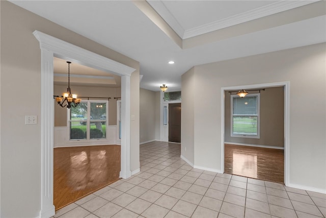 empty room featuring light hardwood / wood-style floors, ornamental molding, a tray ceiling, and a notable chandelier