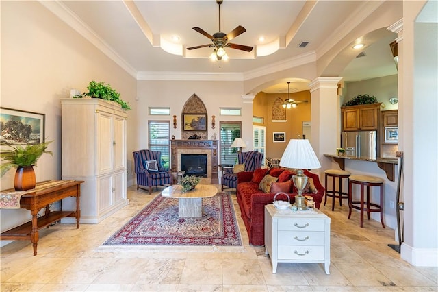 living room featuring ceiling fan, ornamental molding, a raised ceiling, and decorative columns