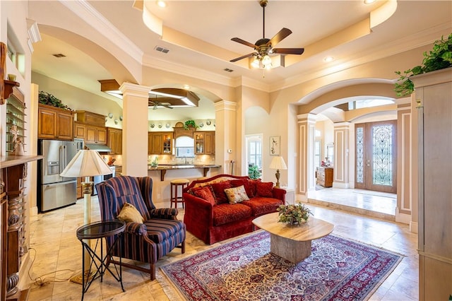 living room with french doors, crown molding, a raised ceiling, ceiling fan, and decorative columns