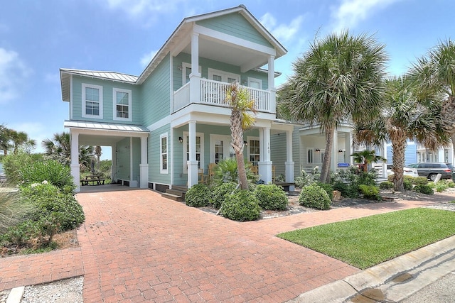 view of front facade featuring a standing seam roof, decorative driveway, covered porch, metal roof, and a balcony