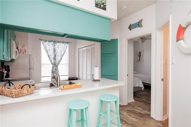 kitchen featuring sink, a kitchen breakfast bar, green cabinets, kitchen peninsula, and light wood-type flooring