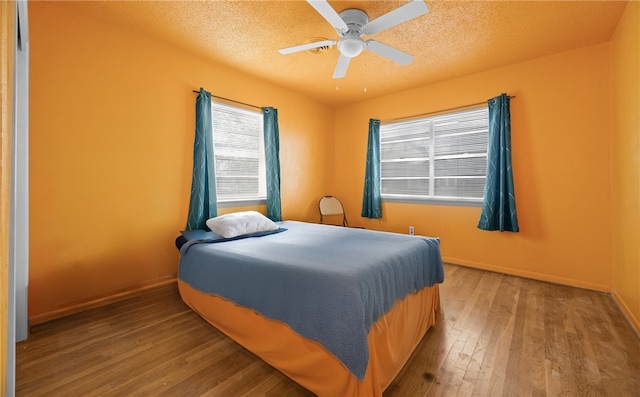 bedroom with ceiling fan, wood-type flooring, and a textured ceiling