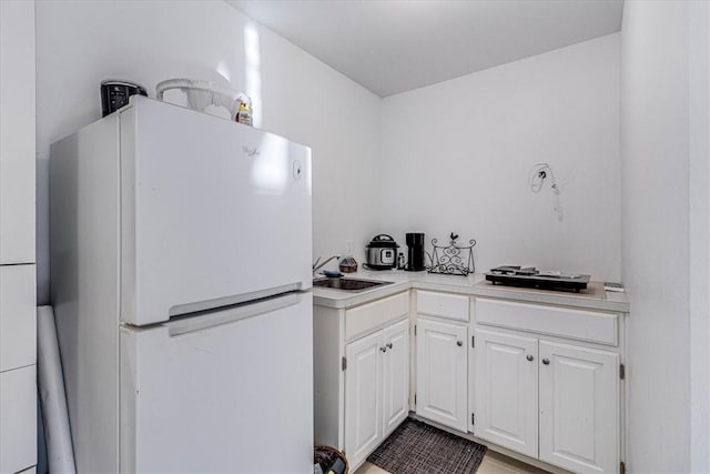 kitchen featuring white cabinets, a sink, light countertops, and freestanding refrigerator