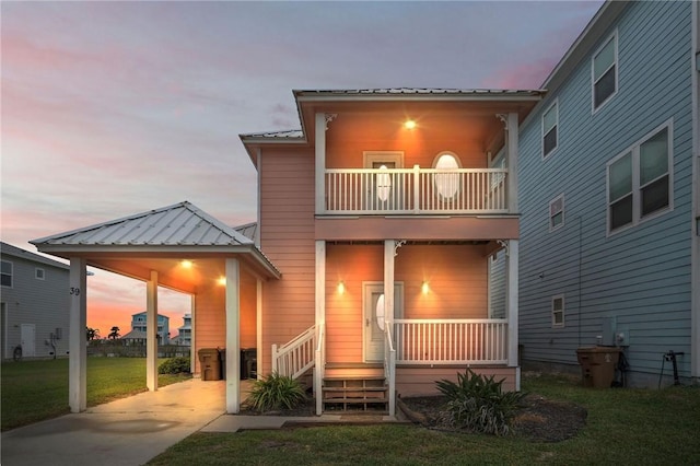 back house at dusk with a balcony, a carport, a lawn, and a porch