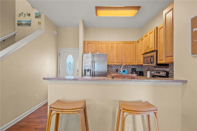 kitchen with backsplash, light brown cabinetry, appliances with stainless steel finishes, and a kitchen breakfast bar