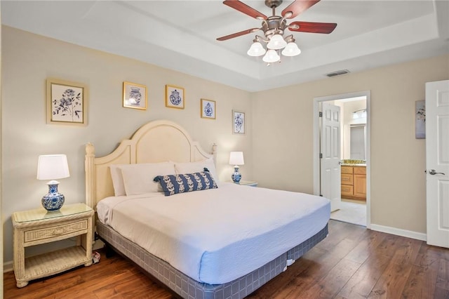 bedroom featuring ceiling fan, dark wood-type flooring, ensuite bathroom, and a raised ceiling