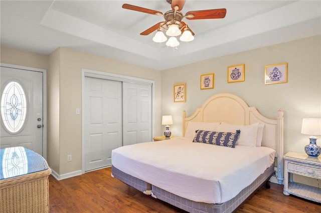 bedroom with a closet, ceiling fan, dark hardwood / wood-style flooring, and a tray ceiling