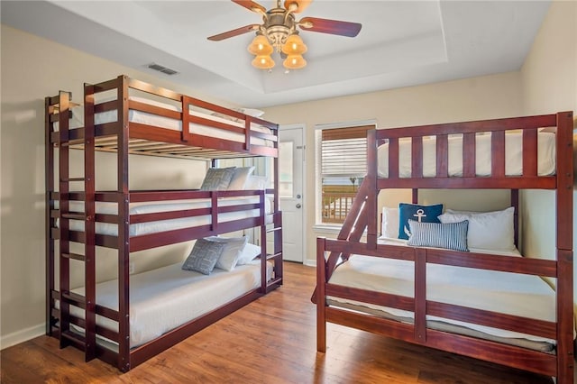 bedroom with ceiling fan, wood-type flooring, and a tray ceiling