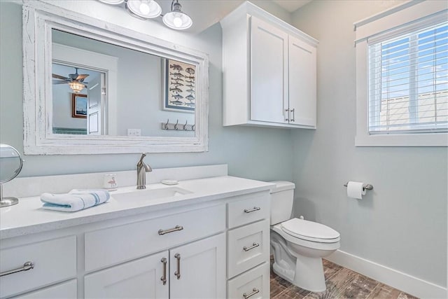 bathroom with toilet, ceiling fan, vanity, wood finished floors, and baseboards