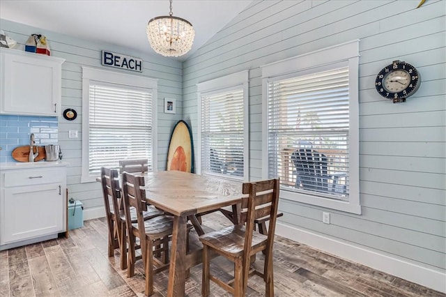 dining room with wooden walls, baseboards, vaulted ceiling, light wood-type flooring, and an inviting chandelier