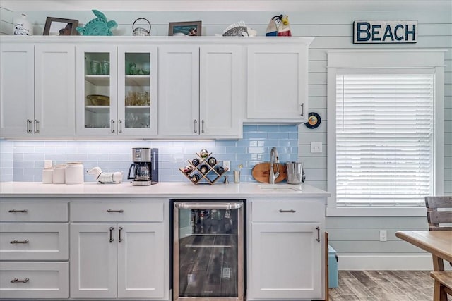 bar featuring tasteful backsplash, beverage cooler, light wood-style flooring, and baseboards