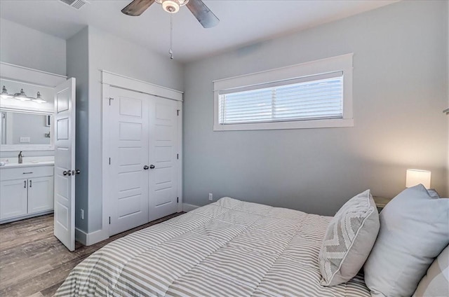 bedroom with a closet, ceiling fan, wood finished floors, ensuite bathroom, and a sink