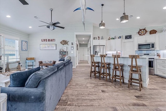 living room with light wood finished floors, visible vents, lofted ceiling, ceiling fan, and wood walls