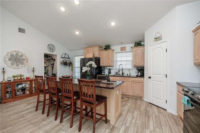 kitchen featuring stainless steel range with electric stovetop, a center island, a kitchen bar, light brown cabinetry, and black fridge