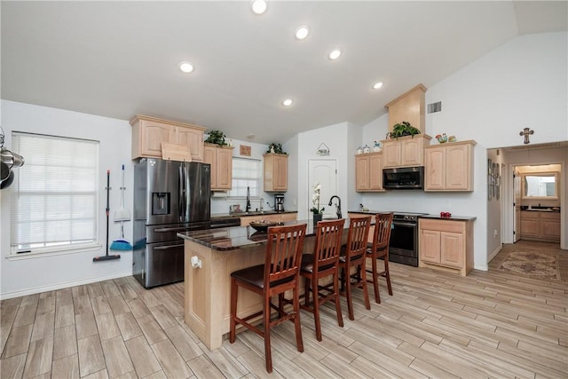 kitchen featuring stainless steel appliances, light brown cabinetry, an island with sink, and a breakfast bar area