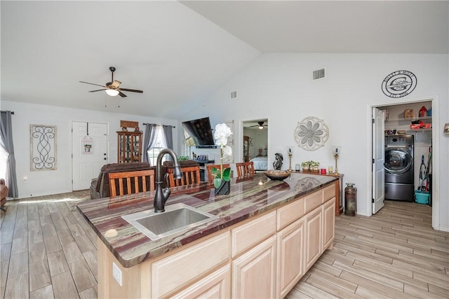 kitchen with washer / dryer, sink, vaulted ceiling, ceiling fan, and a kitchen island with sink