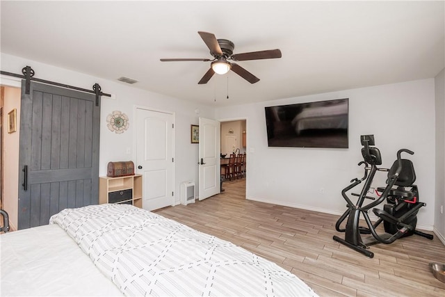 bedroom featuring a barn door, wood finished floors, a ceiling fan, visible vents, and baseboards