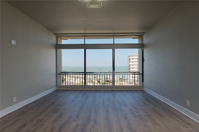 unfurnished room featuring floor to ceiling windows, a water view, and dark hardwood / wood-style flooring