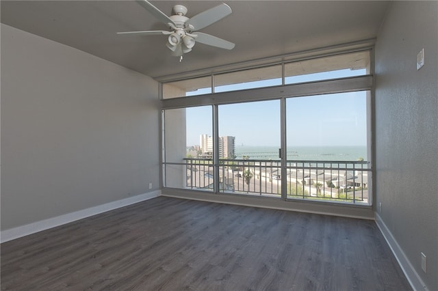 empty room featuring a wealth of natural light, ceiling fan, a water view, and dark hardwood / wood-style flooring