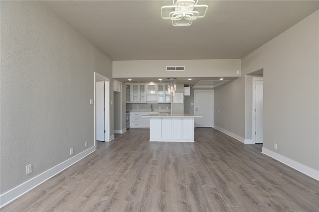 kitchen with a center island, hanging light fixtures, a notable chandelier, white cabinetry, and light hardwood / wood-style flooring