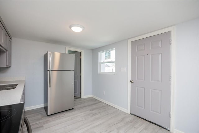 kitchen featuring gray cabinets, stainless steel fridge, light wood-type flooring, and range